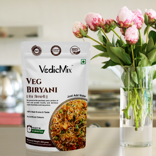 A packaged product of VedicMix Veg Biryani displayed on a kitchen counter with a vase of pink flowers in the background.