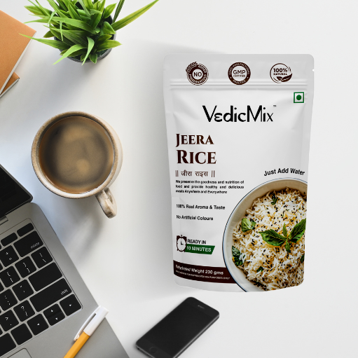 A packaged product of VedicMix Jeera Rice displayed on a desk next to a laptop, a cup of coffee, and a smartphone.